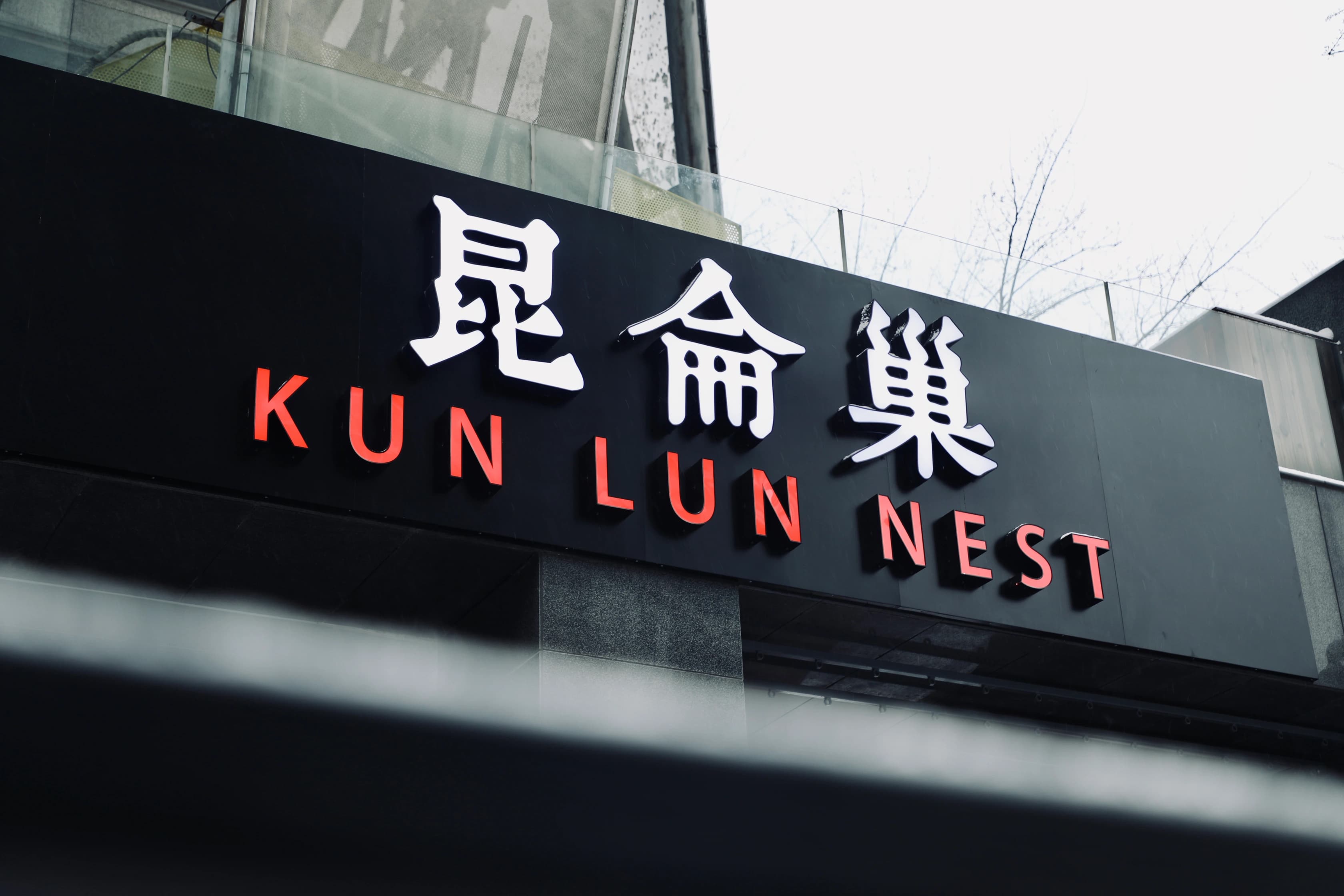 昆仑巢标识牌,白色汉字“昆仑巢”和红色英文“KUN LUN NEST”字样,悬挂在建筑物的黑色背景墙上。